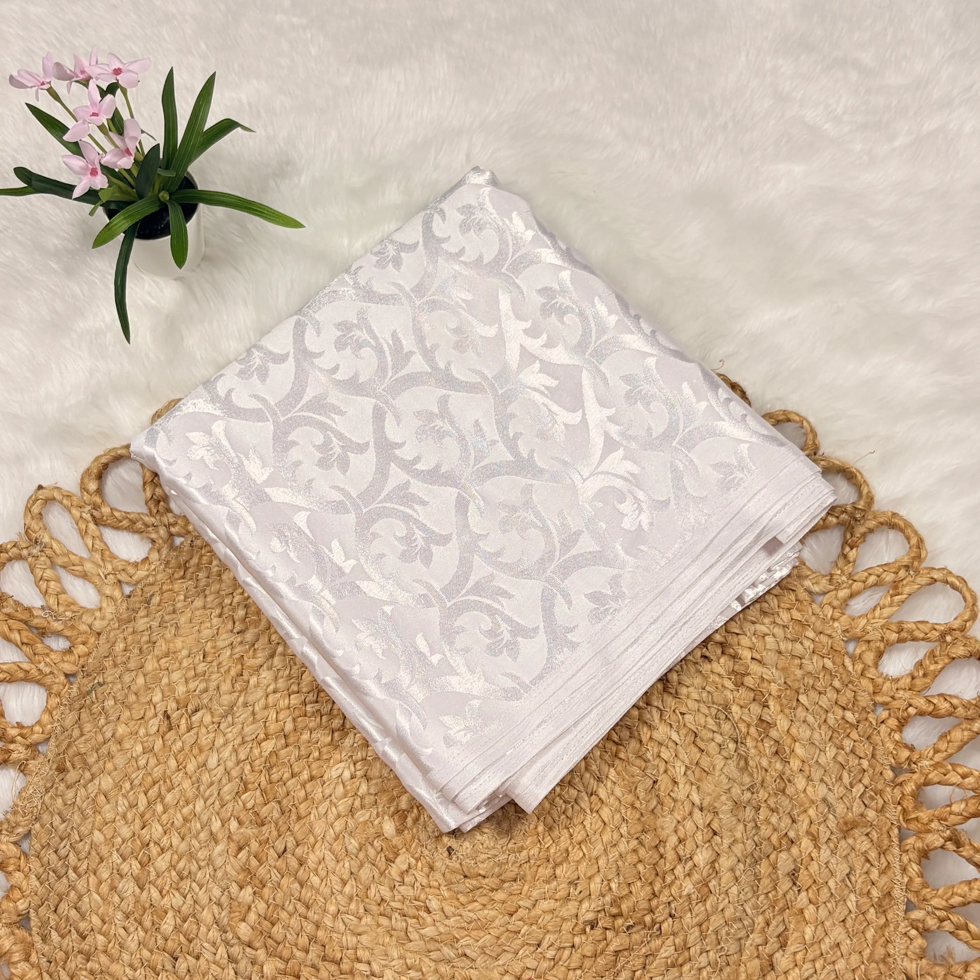 White floral-patterned fabric on a textured surface with a small plant.