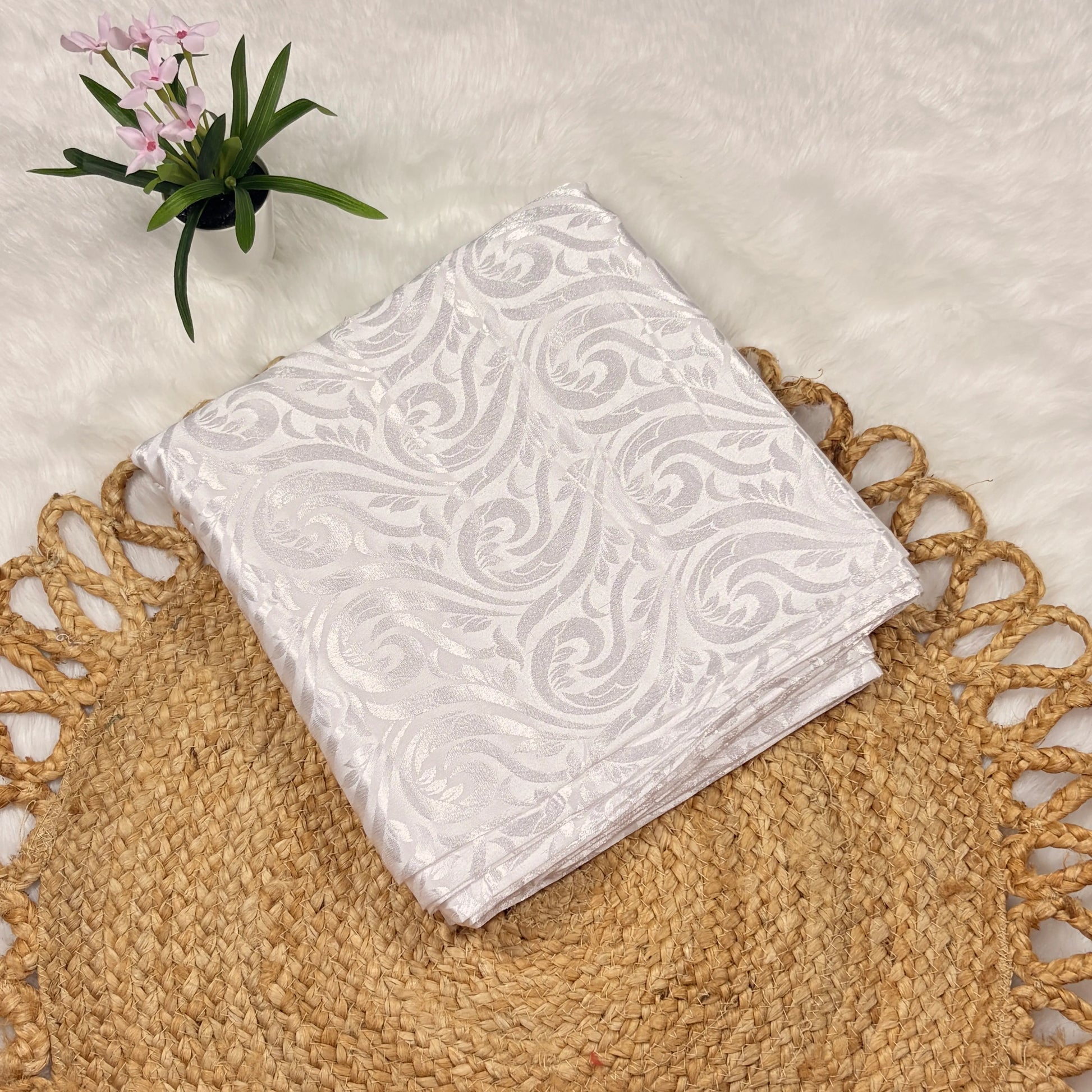 White patterned napkin on a textured surface with a plant in the corner