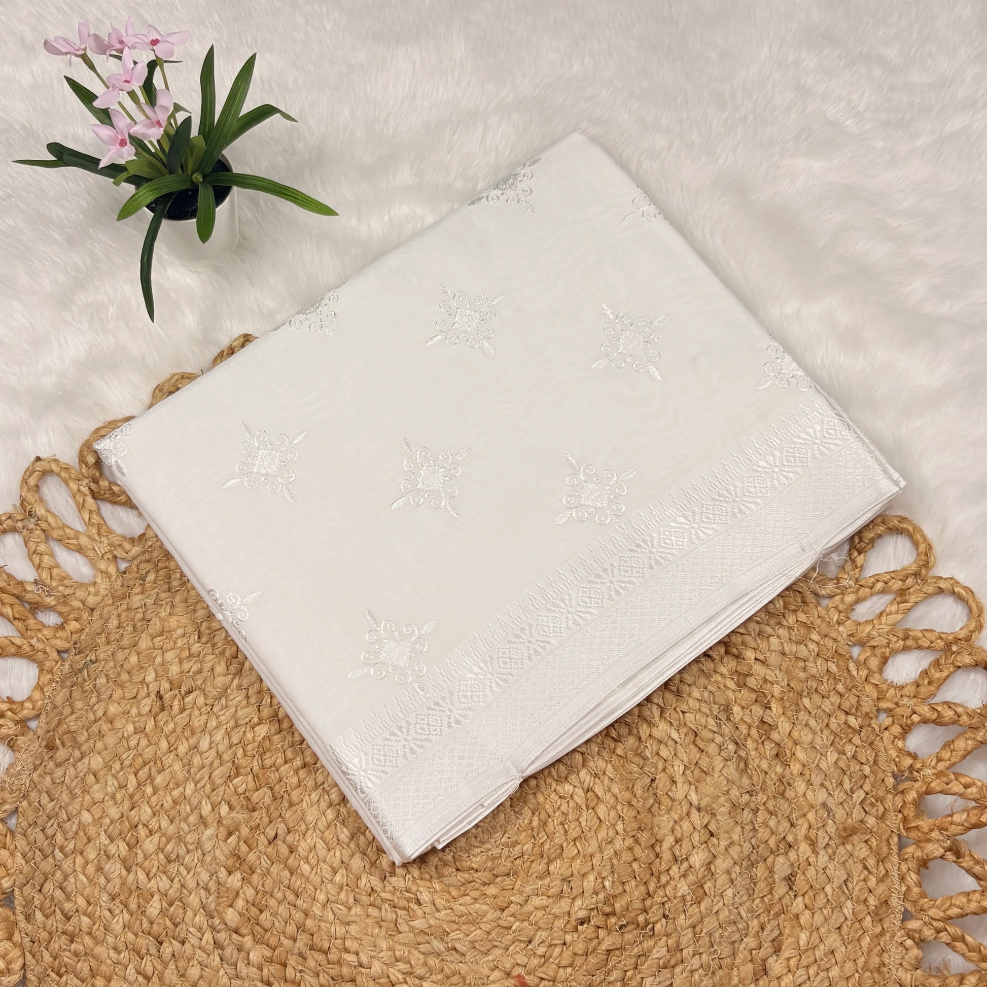 White embroidered fabric on a textured surface with a small plant