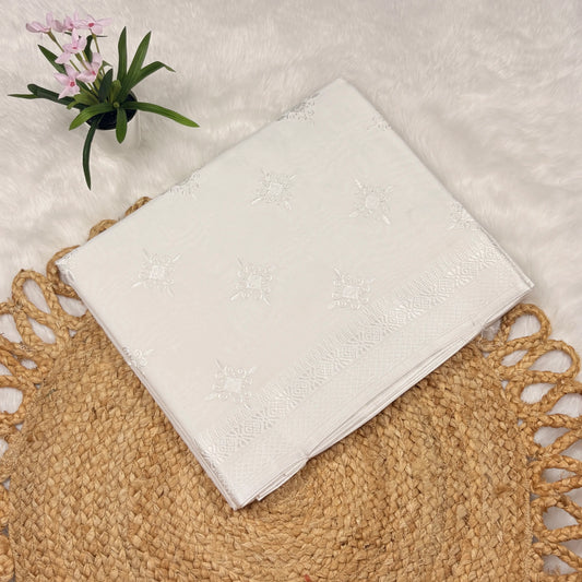 White embroidered fabric on a textured surface with a small plant
