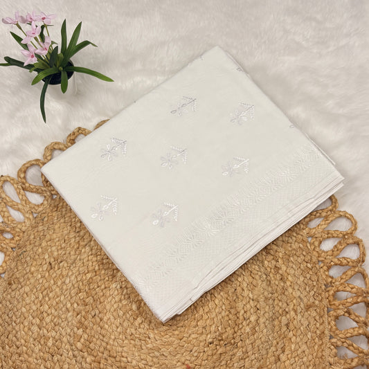 White embroidered fabric on a textured surface with a plant in the corner