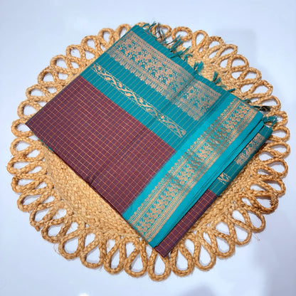 Teal and maroon saree with gold patterns on a decorative woven mat